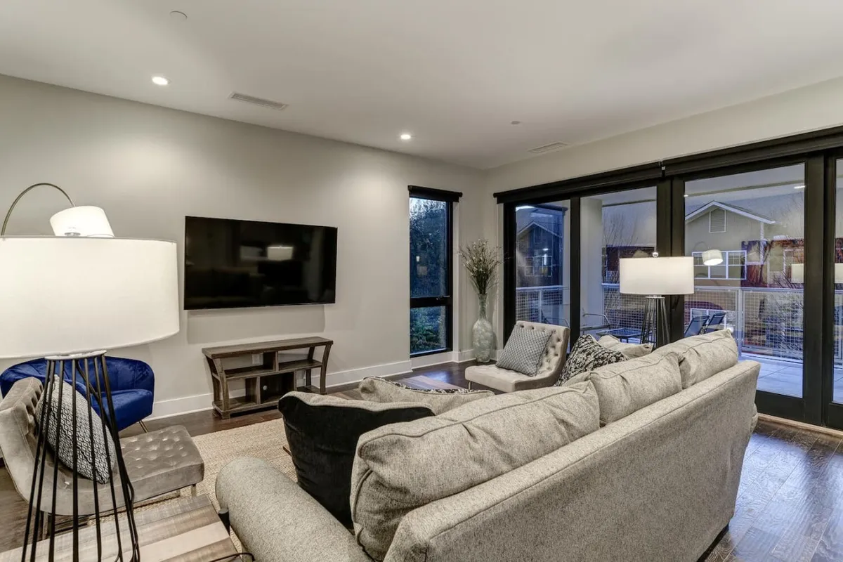A comfortable living room with a sofa, television, lamp, and large windows that let in ample natural light and suggest views of the outdoors. The décor creates a welcoming space for relaxing after a day of exploration.