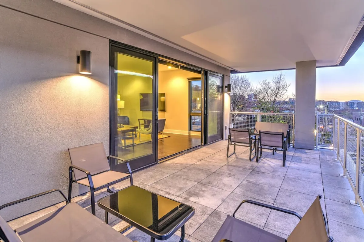 An elevated balcony scene showcases a stylish seating area facing the cityscape. Glass doors seamlessly connect the balcony with the interior, blurring the line between indoor comfort and outdoor relaxation. The city view adds vibrancy, while the setup invites guests to enjoy morning coffee or evening drinks.